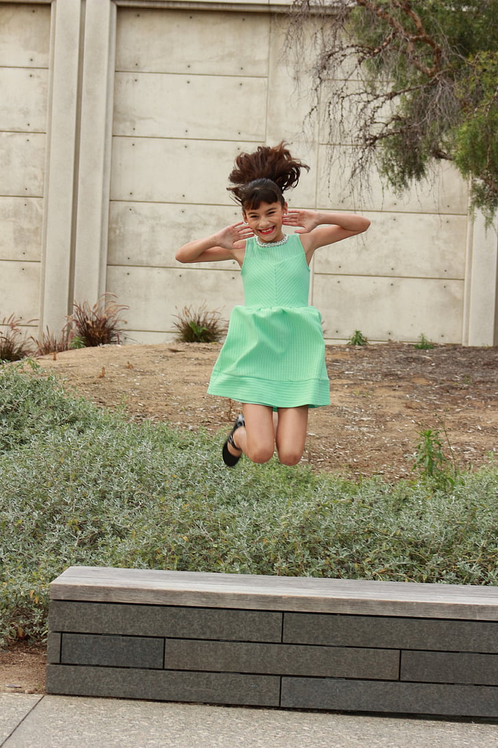 girl jumping beside gray concrete bench