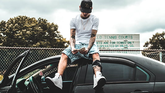 man sitting on sedan's roof near gray fence under gray sky during daytime thumbnail