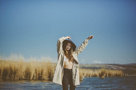 woman raising hand standing on below knee body of water during daytime thumbnail