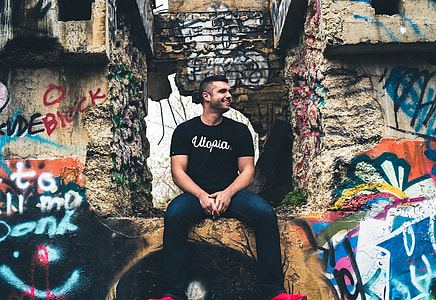 man wearing black utopia text-printed shirt while sitting on ledge thumbnail