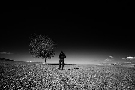 grayscale photography of man wearing jacket near tree thumbnail