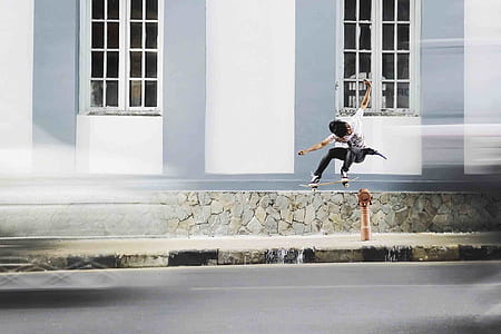 man riding skateboard jumping above post near white concrete building during daytime thumbnail