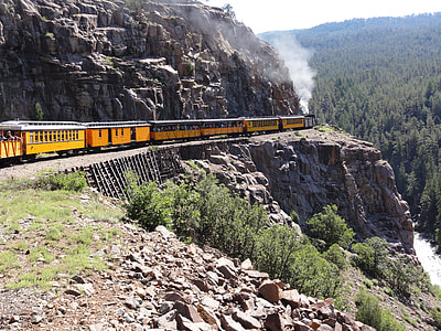 yellow train near cliff surrounded by trees photo thumbnail