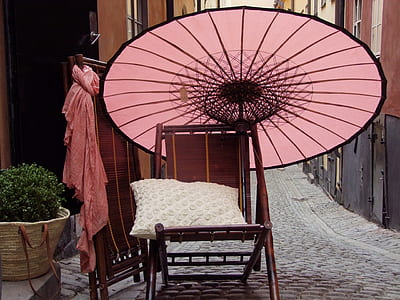 brown wooden chair and pink umbrella near alley during daytime thumbnail