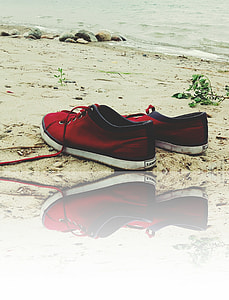 pair of red and black shoes on beach sand at daytime thumbnail