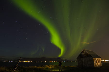 person standing near body of water and brown shack thumbnail