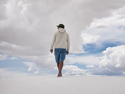man on white sand wearing white hooded jacket and blue shorts thumbnail