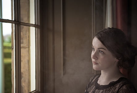 woman in black dress standing near window thumbnail