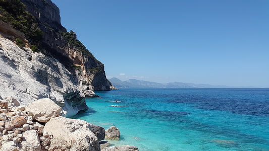 rock cliff near body of water under blue sky thumbnail
