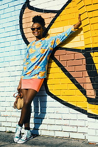 woman smiling and posing for picture while leaning on yellow and white muraled wall during daytime thumbnail