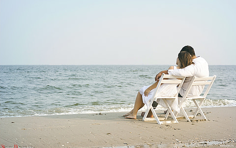 man and woman sitting on white wooden chairs beside the shore thumbnail