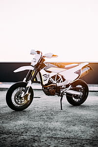 white and black dirt bike parked on gray concrete pavement thumbnail