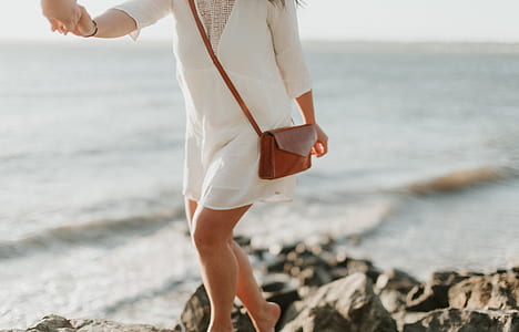 woman walking on black rock formation near ocean thumbnail