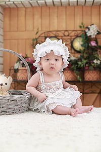 toddler in white dress sitting beside basket thumbnail