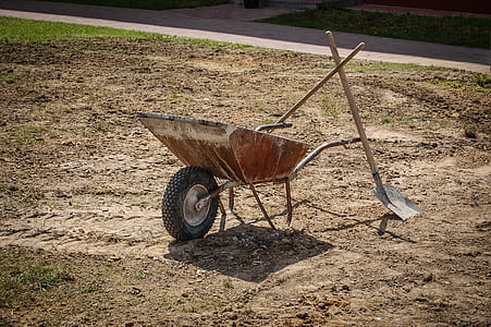 two brown shovels leaning on brown wheelbarrow on brown soil at daytime thumbnail