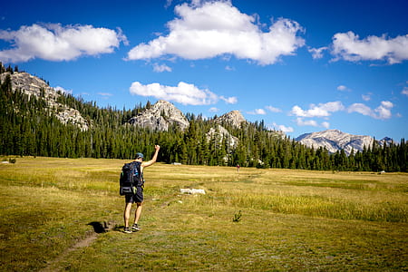 man wearing black backpack walking on green grass during daytime thumbnail