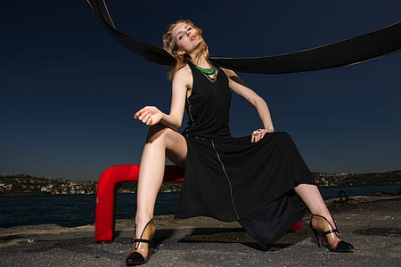 woman wearing black sleeveless midi dress sitting on red metal pole during nighttime thumbnail