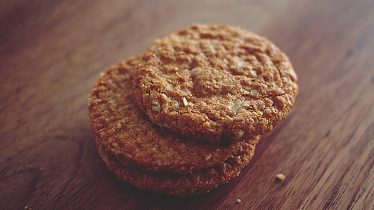 three brown cookies stacked on top of one another placed on brown wooden surface thumbnail