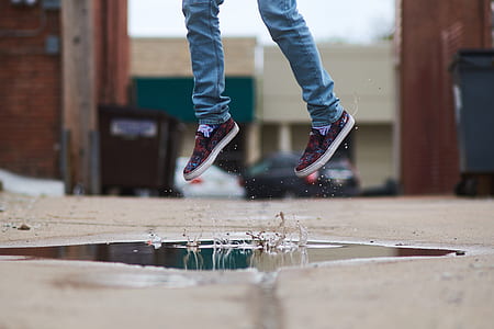 person wearing blue denim skinny pants and red shoes jumping on beige surface thumbnail