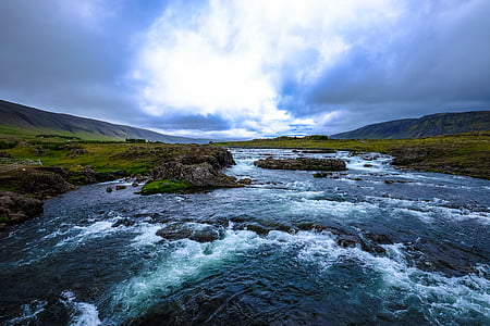 river in between grass field under blue sky at daytime thumbnail