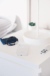 silver iPhone 7 beside silver Apple TV remote on white wooden nightstand thumbnail
