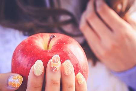 woman holding apple fruit with orange french tip accent manicure in closeup photography thumbnail