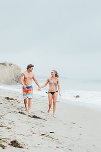 man and woman holding hand while walking at the beach thumbnail