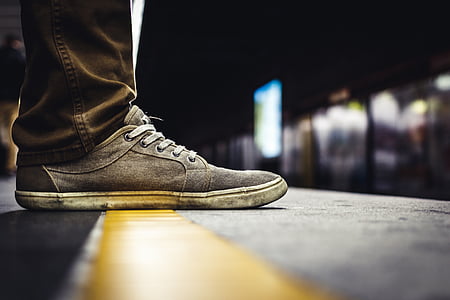 selective focus photo of person wearing gray and white suede low-top shoe and brown jeans over gray and yellow concrete ground thumbnail