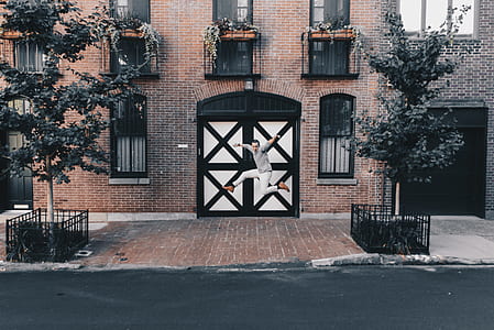 man jumping besides white and black wooden door between trees during daytime thumbnail