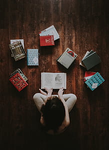 woman sitting with crossed legs surrounded with book lot on brown parquet thumbnail