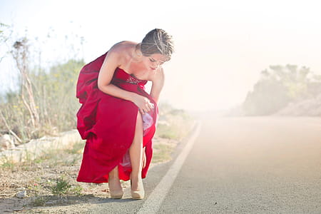 Young Adult Woman In Red Party Gown Dress Adjusting Her Shoes During Photo Shoot thumbnail