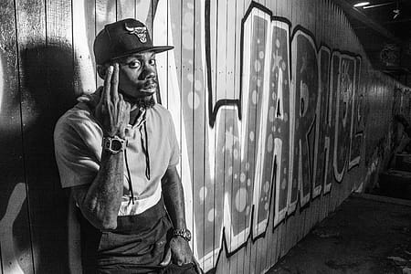 Grayscale Photo of Man Leaning On Wall With Graffiti thumbnail