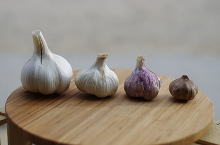 four assorted-size-and-color garlic bulbs on brown chopping board thumbnail