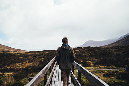 man standing on wooden bridge near mountain range thumbnail