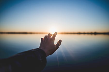 man reaching sun rays on body of water thumbnail