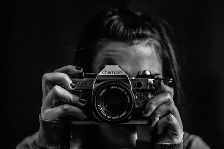 grayscale photography of woman holding Canon DSLR camera thumbnail