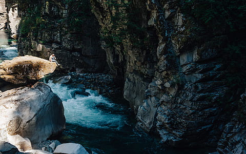person sitting on top of cliff near body of water during daytime thumbnail