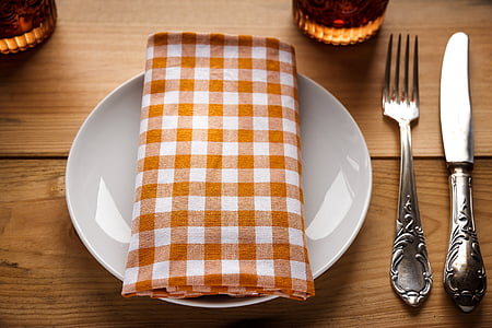 orange and white gingham tablecloth on round white ceramic plate beside fork and knife thumbnail