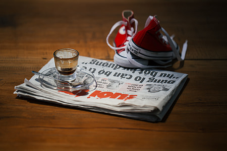 glass teacup on newspaper beside pair of red shoes thumbnail