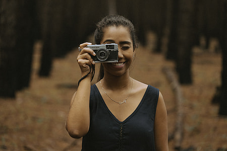 woman holding camera near trees thumbnail