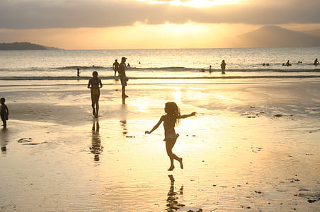 silhouette of girl playing on seashore near people on beach during sunset thumbnail