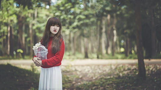 woman wearing red long-sleeved top and white skirt holding white metal bird cage thumbnail