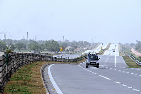 black vehicle on road in distant of trees thumbnail