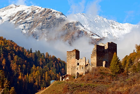 beige concrete ruins surrounded with tall trees near snow capped mountain at daytime thumbnail
