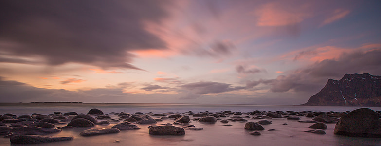 rocks on shore with distance to mountain during sunrise thumbnail