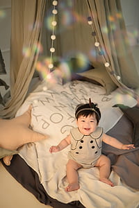 baby sitting on white bed sheet thumbnail