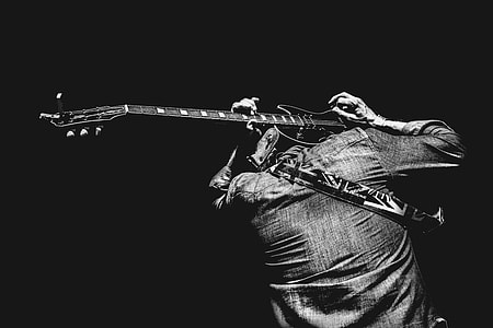 grayscale photo of man holding guitar on his head thumbnail