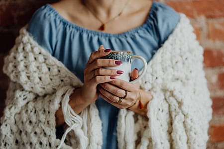 A woman in a warm blanket holds a cup of coffee or tea thumbnail