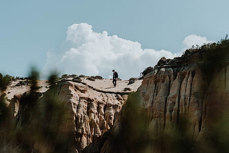 man standing above brown rock cliff under white cloudy skies at daytime thumbnail