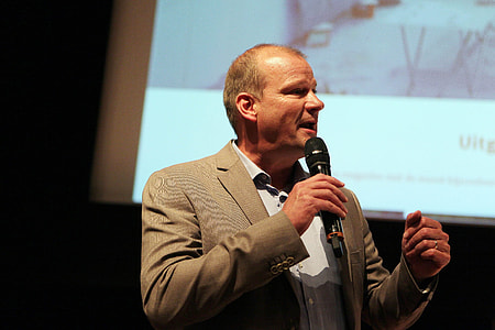 man standing near projector screen while holding microphone thumbnail